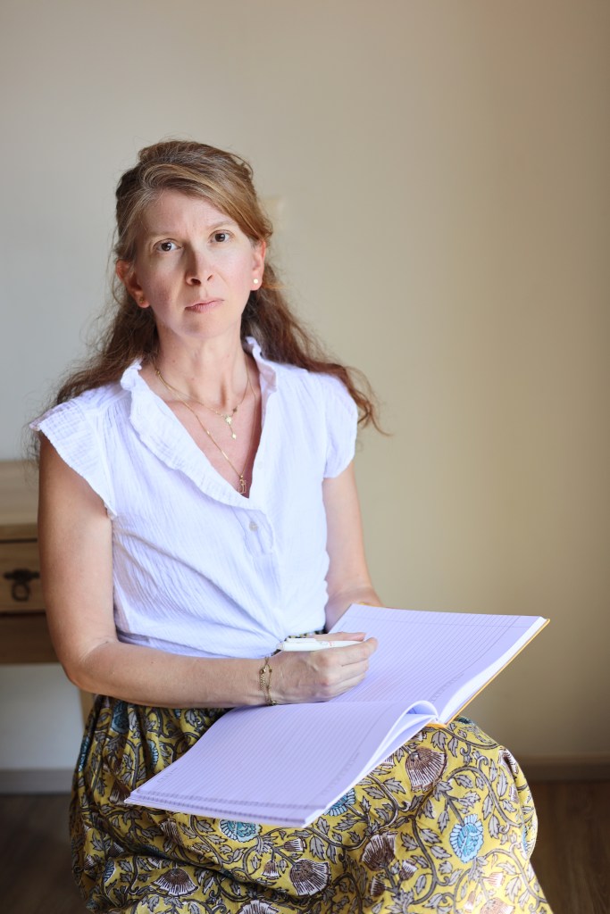 Sandrine Muggéo assise avec un carnet sur les genoux dans un espace de consultation